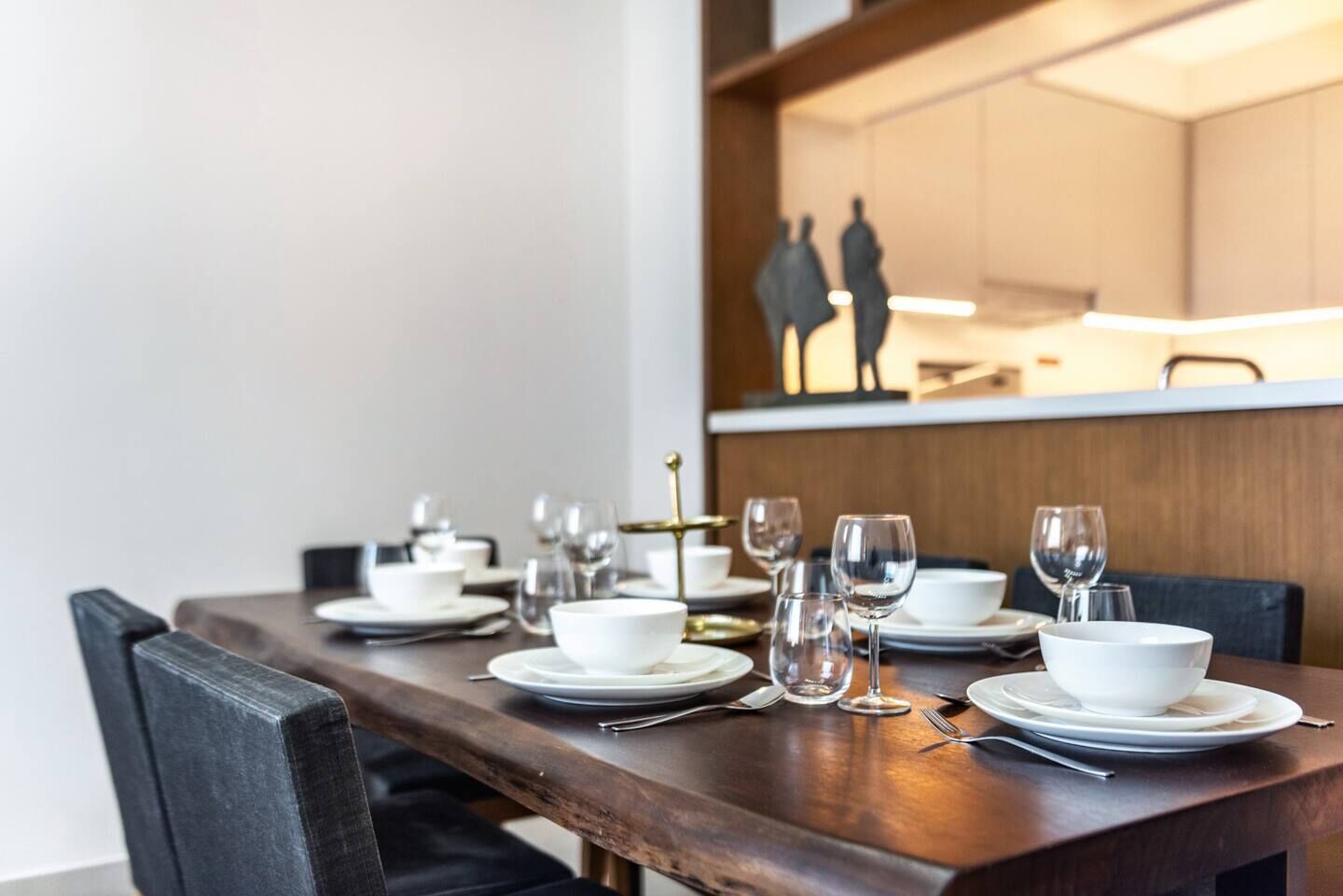 A dining table set with white plates, bowls, and wine glasses, with chairs on either side.