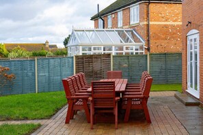 A patio with a wooden table and chairs, a conservatory, and a brick house. - 4 Luxurious Executive Villa (Sheerness)
