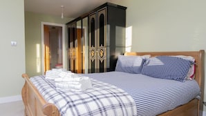 A neatly made bed with a plaid blanket and striped pillows, a wooden headboard, and a black wardrobe with gold handles. - 4 Luxurious Executive Villa (Sheerness)