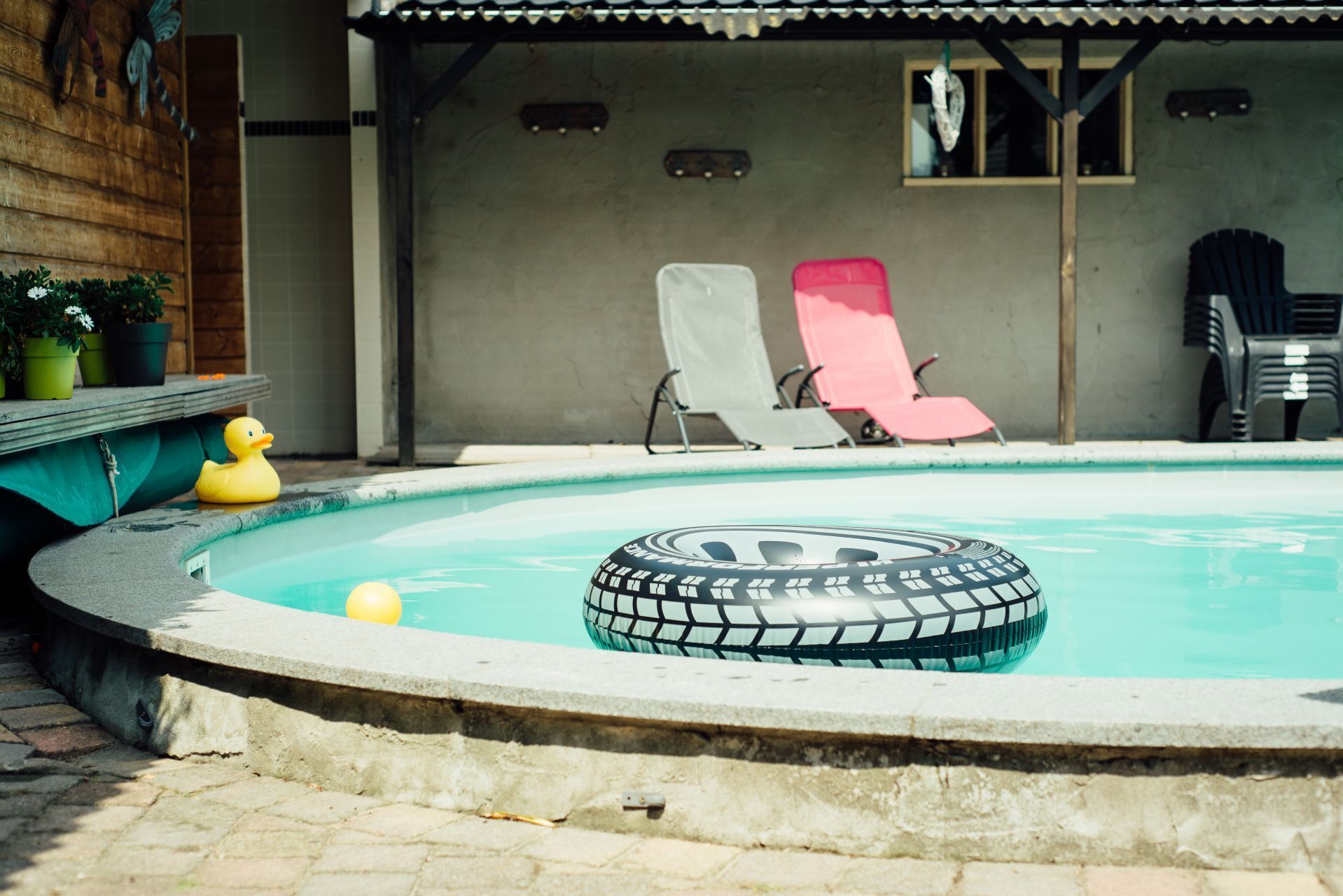 A swimming pool with a tire float, lounge chairs, and potted plants.
