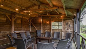 A wooden cabin with a covered patio area featuring wicker furniture and string lights. - Lamperse hei (Wanroij)
