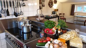 A kitchen with stainless steel appliances, a variety of fresh vegetables, and hanging utensils. - Lamperse hei (Wanroij)