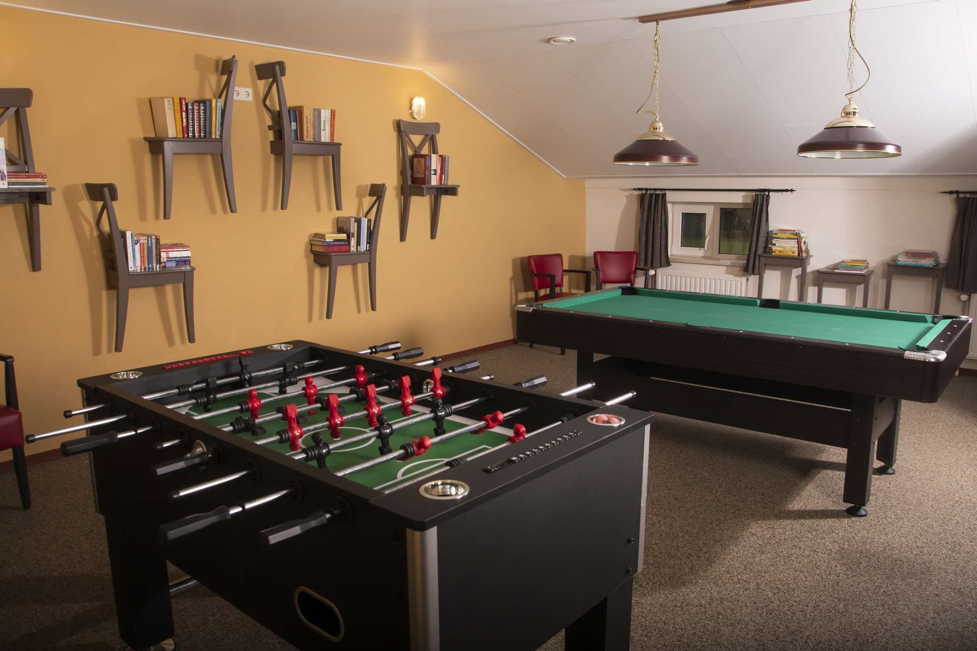 A room with a foosball table, a pool table, and bookshelves against the wall.