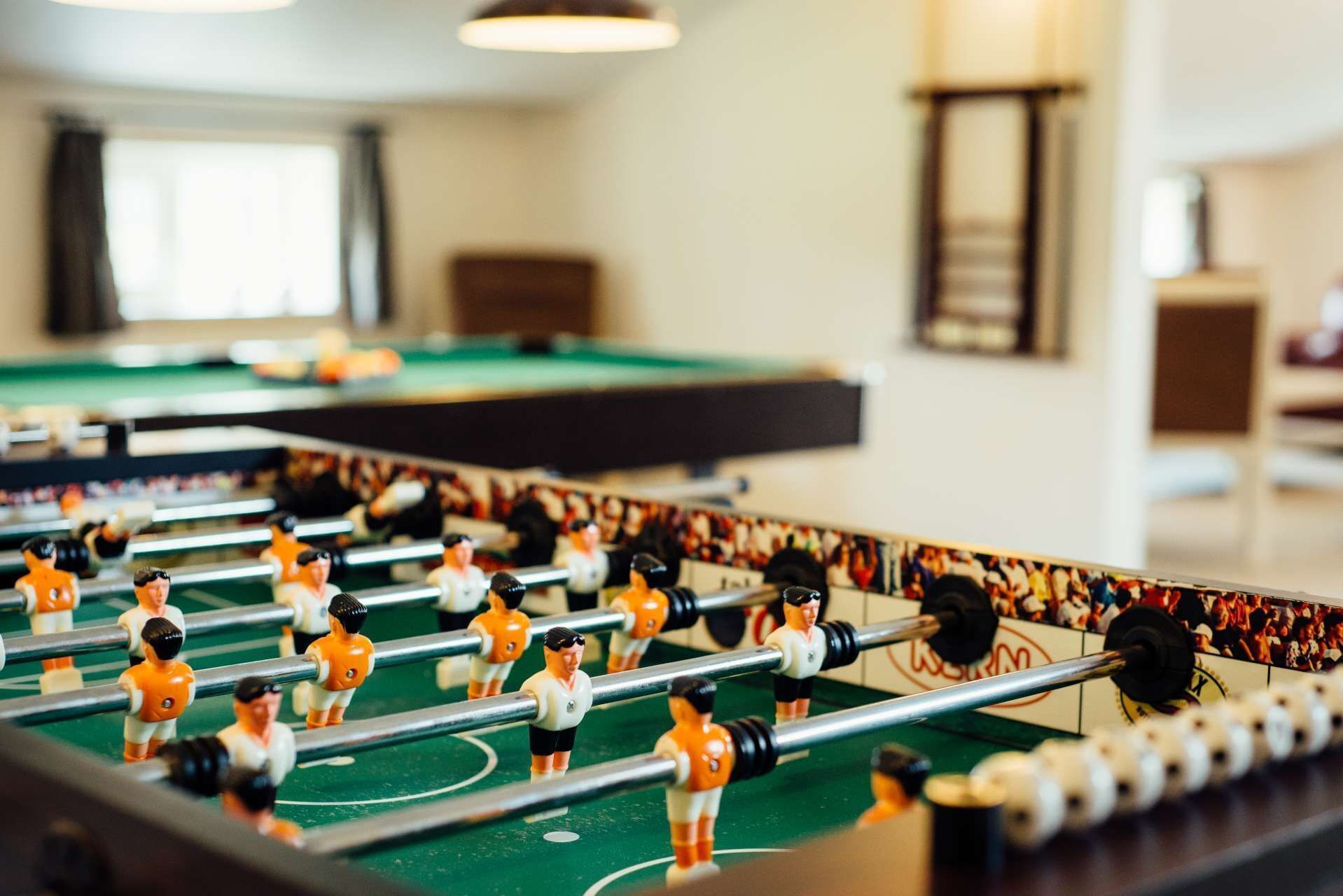 Una mesa de fútbol de mesa en una habitación con una mesa de billar y una mesa de carambola al fondo.