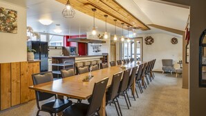 A spacious dining area with a long wooden table and multiple chairs, a kitchen with modern appliances, and a high ceiling with exposed beams. - Lamperse hei (Wanroij)