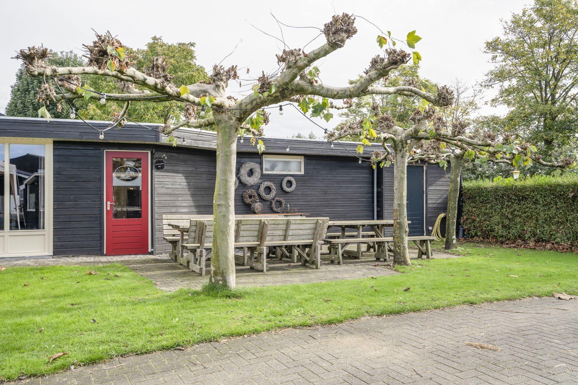 Un bâtiment rustique avec une porte rouge, des bancs en bois et un espace jardin.