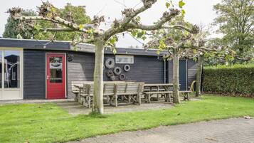 Un bâtiment rustique avec une porte rouge, des bancs en bois et un espace jardin.