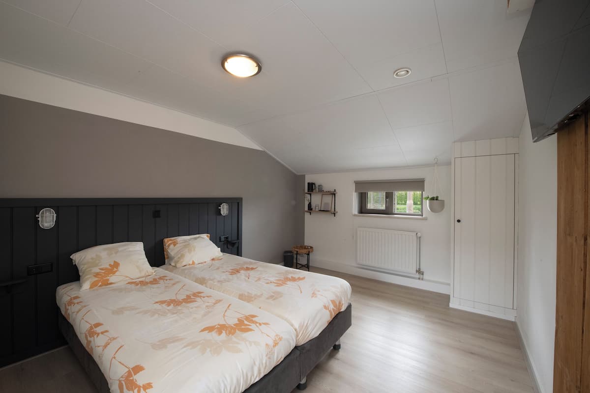 Quarto com uma cama grande, guarda-roupa de madeira e janela com vista para o verde.