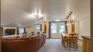 A spacious living area with a brown leather sectional sofa, a wooden dining table with chairs, and a flat-screen TV mounted on the wall. - Lamperse hei (Wanroij)