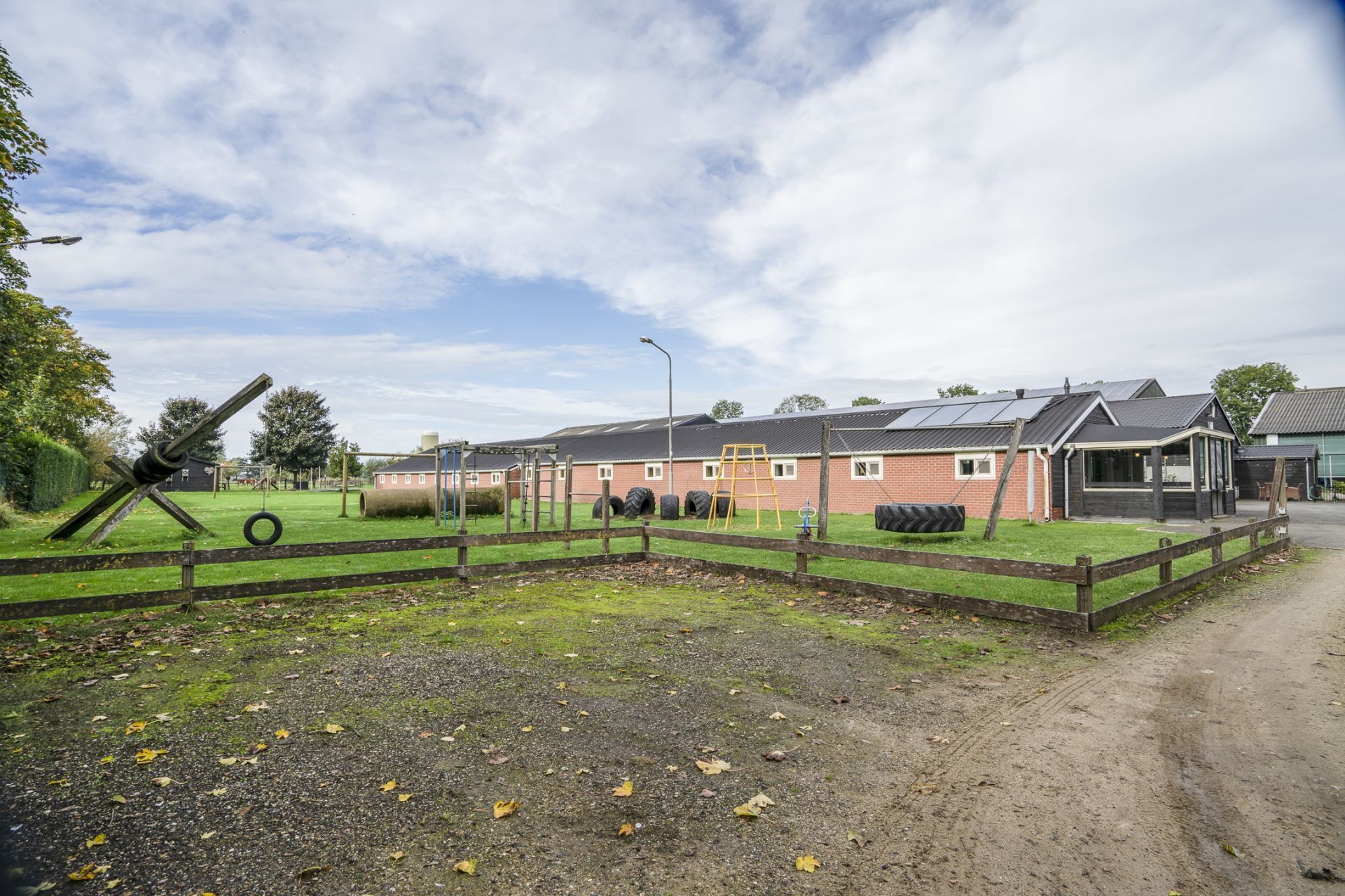 Un paysage rural comprenant une ferme, un enclos avec un tracteur et un chemin de terre.