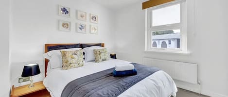 A bedroom with a bed, a nightstand, a lamp, and a window with a view of buildings.