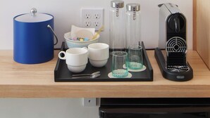 Un comptoir de cuisine avec une machine à café, un récipient bleu, des tasses blanches et des verres transparents.