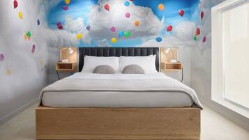 Quarto com cama, duas mesinhas de cabeceira, um criado-mudo e um mural na parede com nuvens e balões.