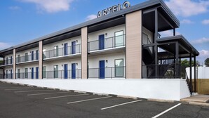 Un bâtiment à deux étages, sur lequel on peut lire l’inscription « ARTELLO ». Il est doté d’un toit plat, de plusieurs balcons et d’un parking situé à l’avant.