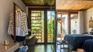 A room with a bed, a table, and a bench. There is a window with a view of greenery outside. - Mayim Villa (Maraú)