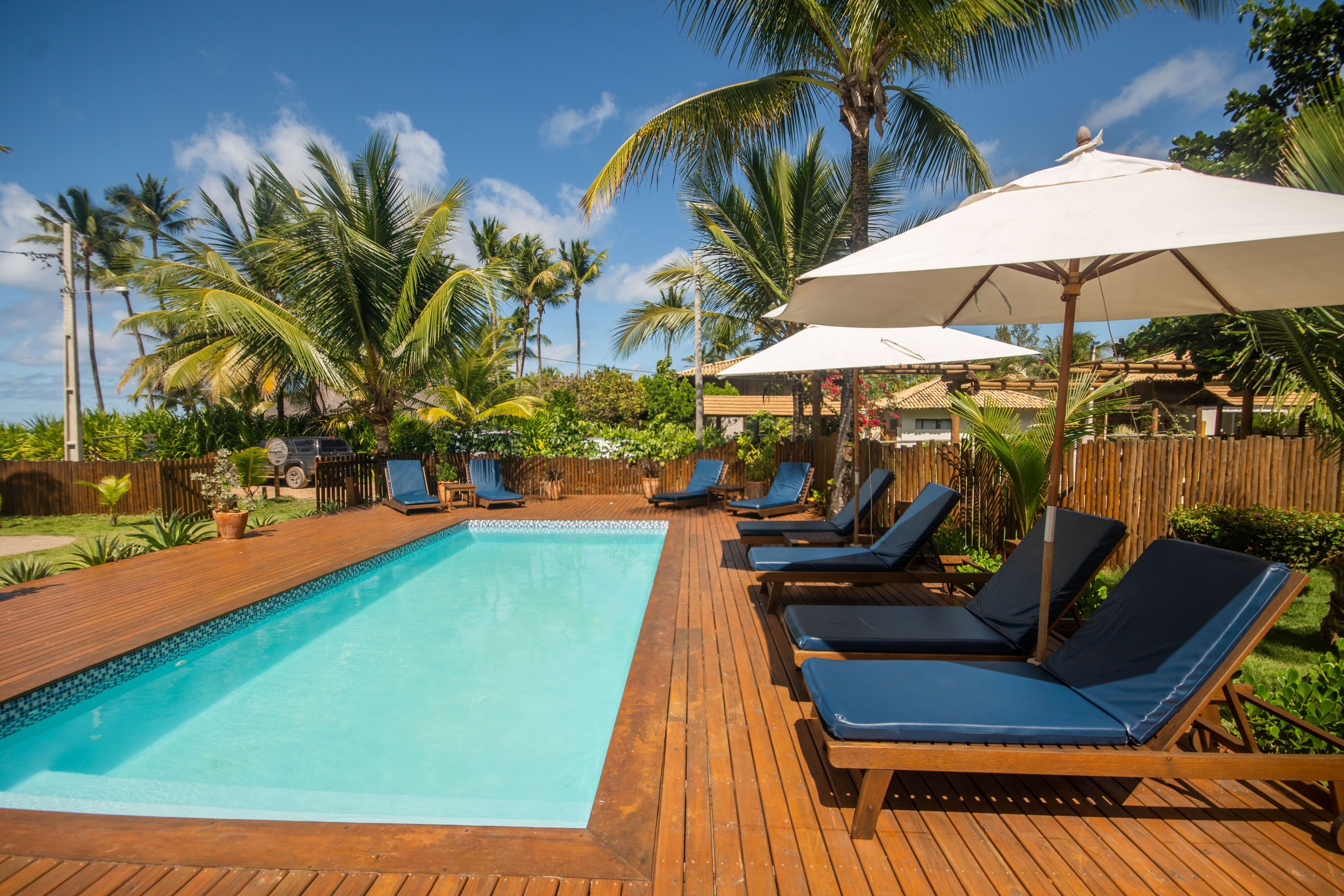 A wooden deck with a swimming pool, lounge chairs, and umbrellas.