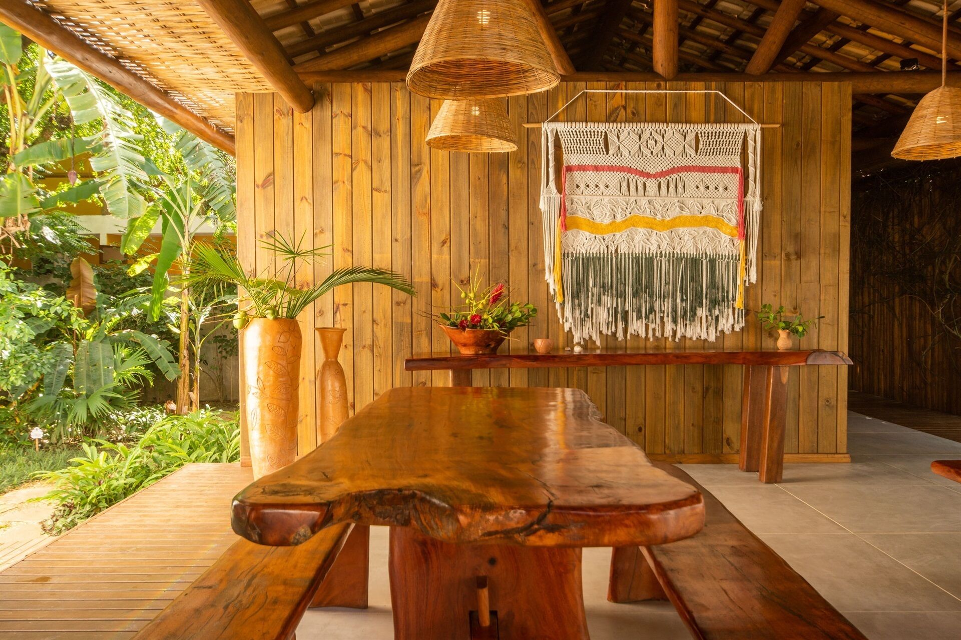 A wooden dining area with a rustic bench, woven hanging lights, and a macramé wall hanging.