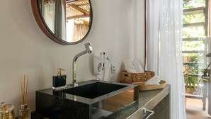A bathroom with a black sink, a mirror, a towel rack, a basket with towels, and a view of greenery outside. - Mayim Villa (Maraú)
