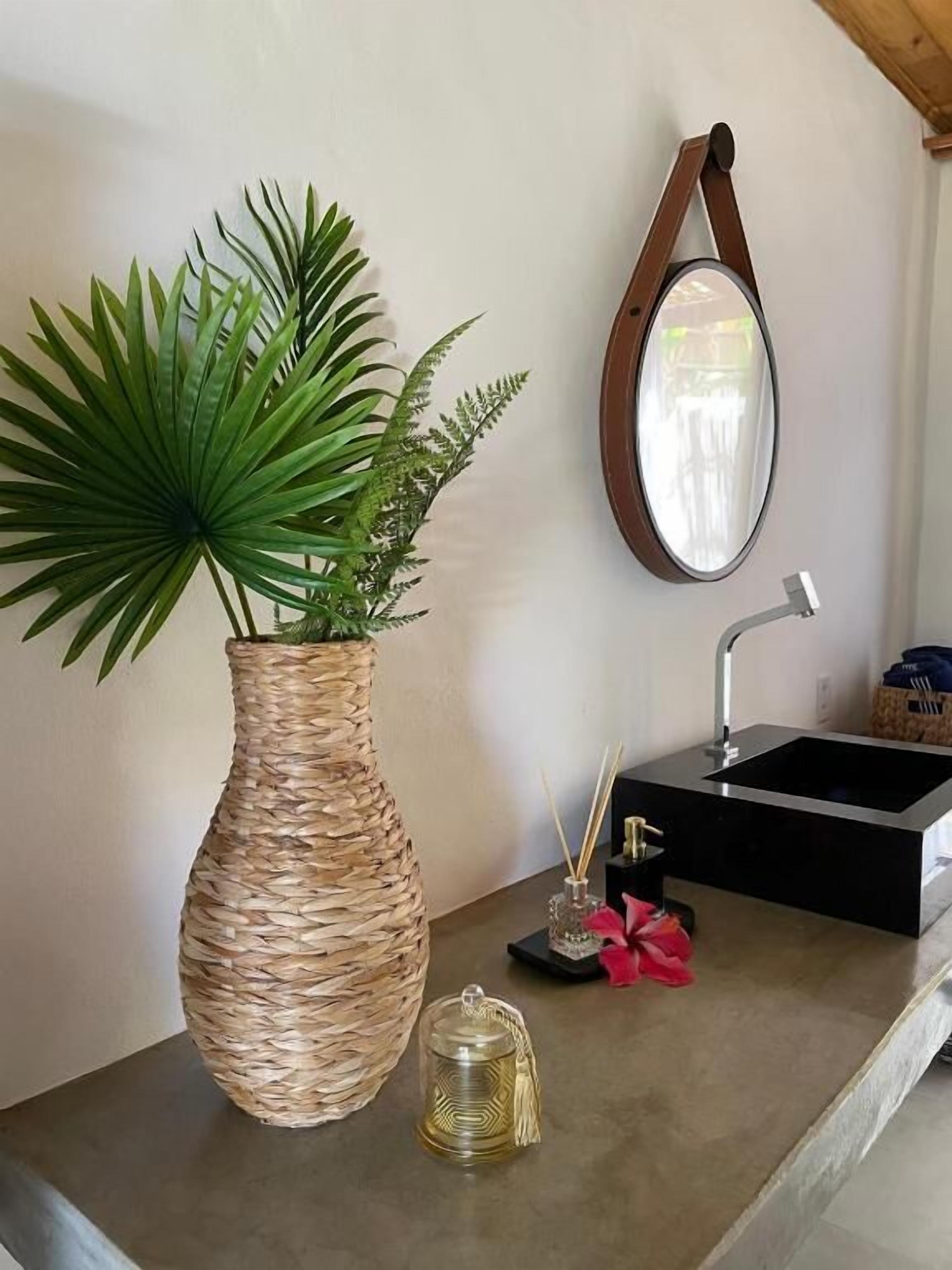A kitchen counter with a woven plant vase, a glass teapot, and a modern sink with a mirror above it.