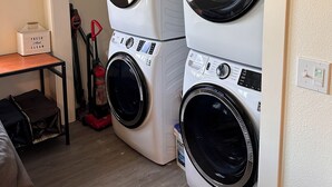 A laundry room with two stacked front-loading washing machines, a vacuum cleaner, and a small table with a basket labeled "FRESH And CLEAN". - The Asbury House Guest Rentals (Moscow)