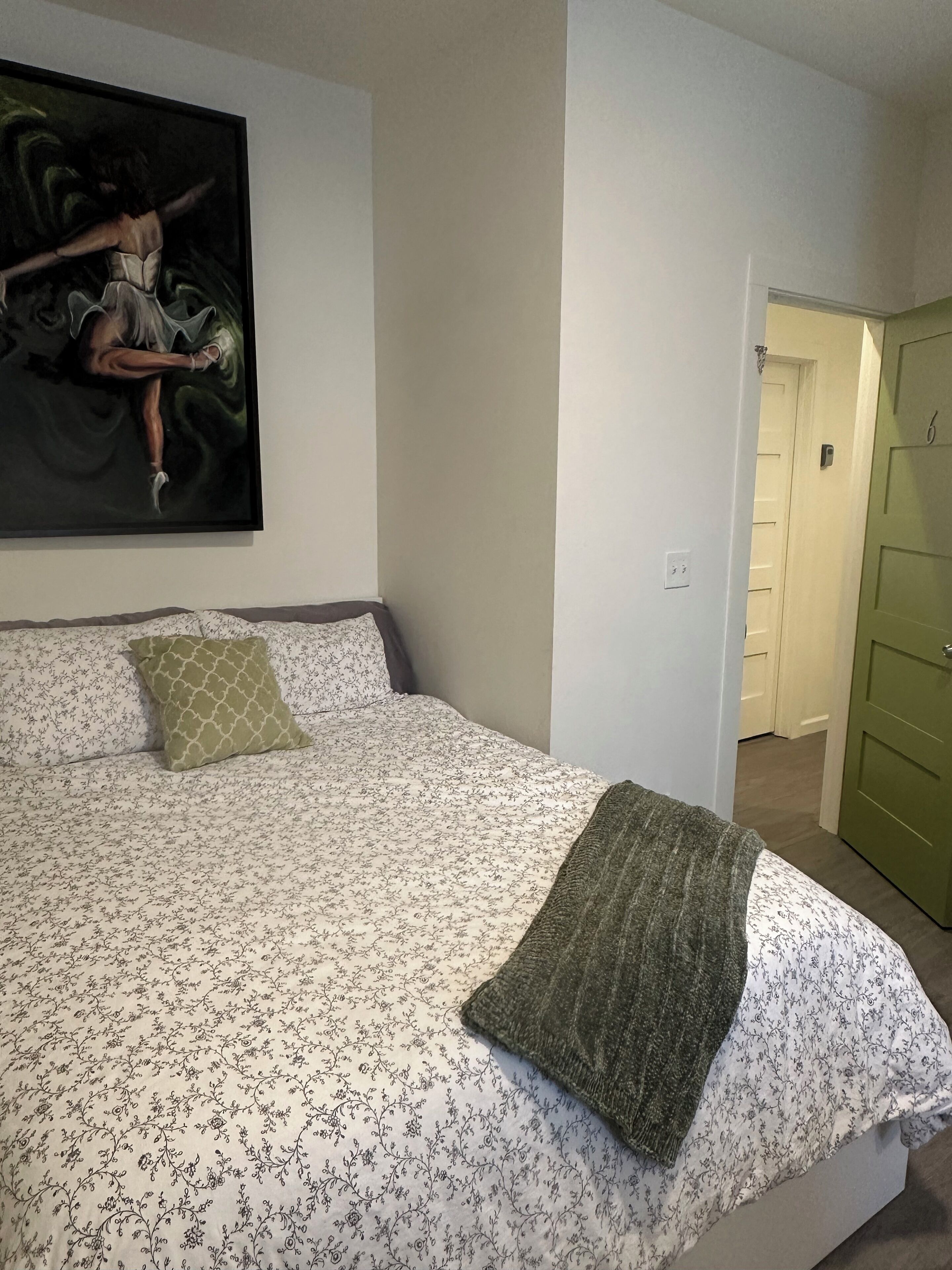 A bedroom with a bed, a green door, and a painting on the wall.