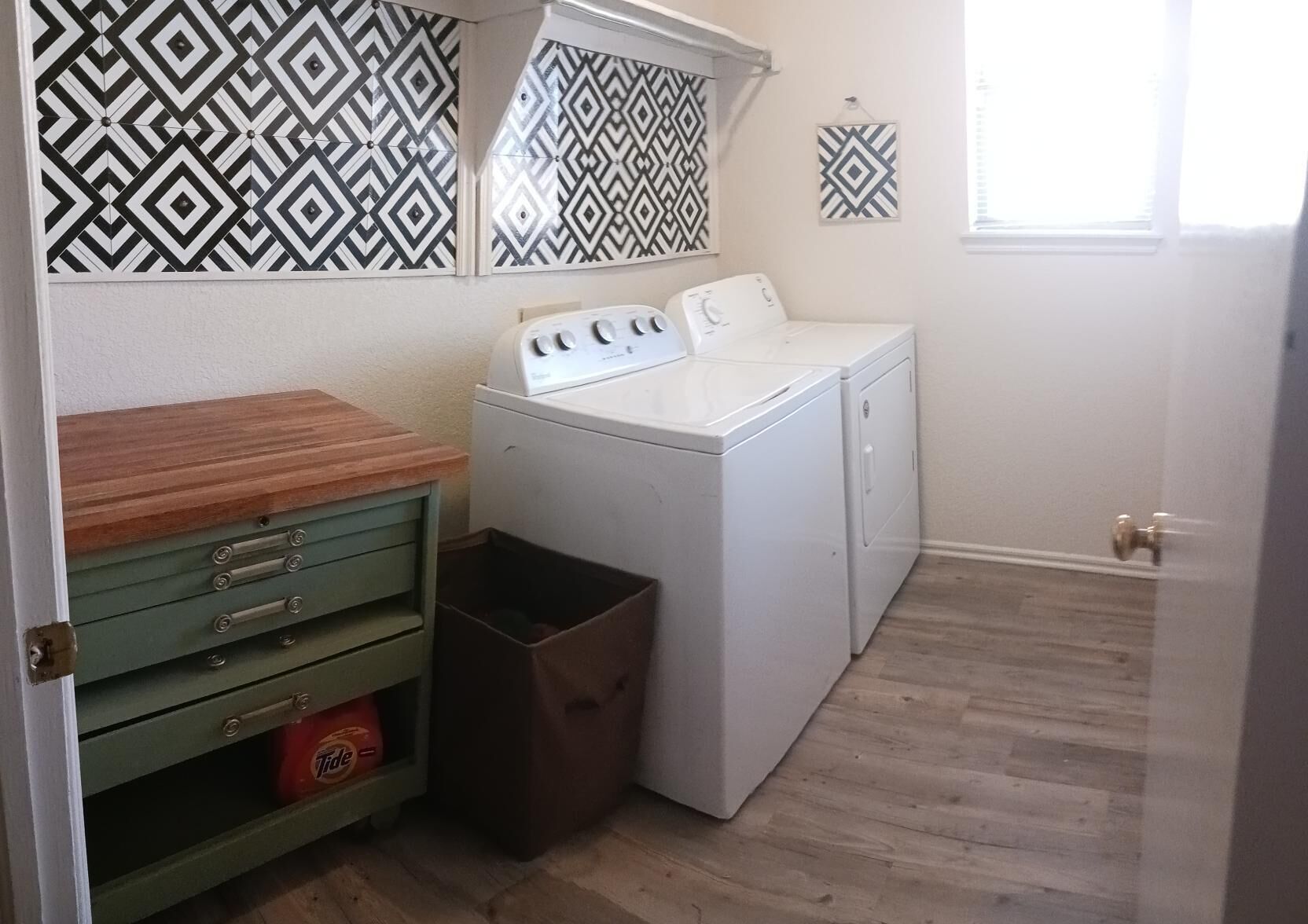 A laundry room with a washing machine, a dryer, a wooden counter, and a trash bin.