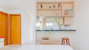 A modern kitchen with a white countertop, wooden cabinets, and a wooden stool. - GB67 Ótimo Apto 2 Suítes - Guarajuba (Camaçari)