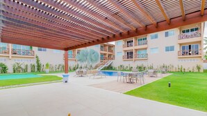 A covered outdoor area with a pool, lounge chairs, and a staircase leading to an upper floor. - GB67 Ótimo Apto 2 Suítes - Guarajuba (Camaçari)