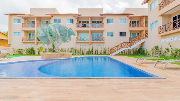 A multi-story hotel with a swimming pool, outdoor seating, and a staircase leading to the upper floors. - GB67 Ótimo Apto 2 Suítes - Guarajuba (Camaçari)
