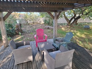 A covered outdoor seating area with wicker furniture and a red chair. - Maison à 50m de L'océan (Yves)