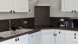 A modern kitchen with white cabinets, a stainless steel range hood, a dishwasher, and a coffee maker. - Maison à 50m de L'océan (Yves)