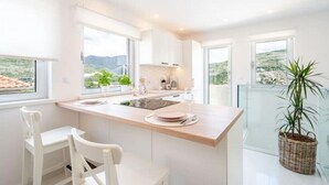 A modern kitchen with a central island, white cabinetry, and large windows offering a view of the landscape. - Villa Diana: Bayside View Beauty - a romantic home
 (Dubrovnik)