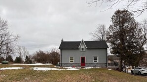 A two-story house with a red door, a grey exterior, and a sloped roof. - Beautiful house on farm, Nature lover's paradise (Rosemont)