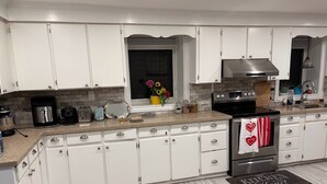 A kitchen with white cabinets, a stainless steel range hood, and a window with a flower arrangement. - Beautiful house on farm, Nature lover's paradise (Rosemont)