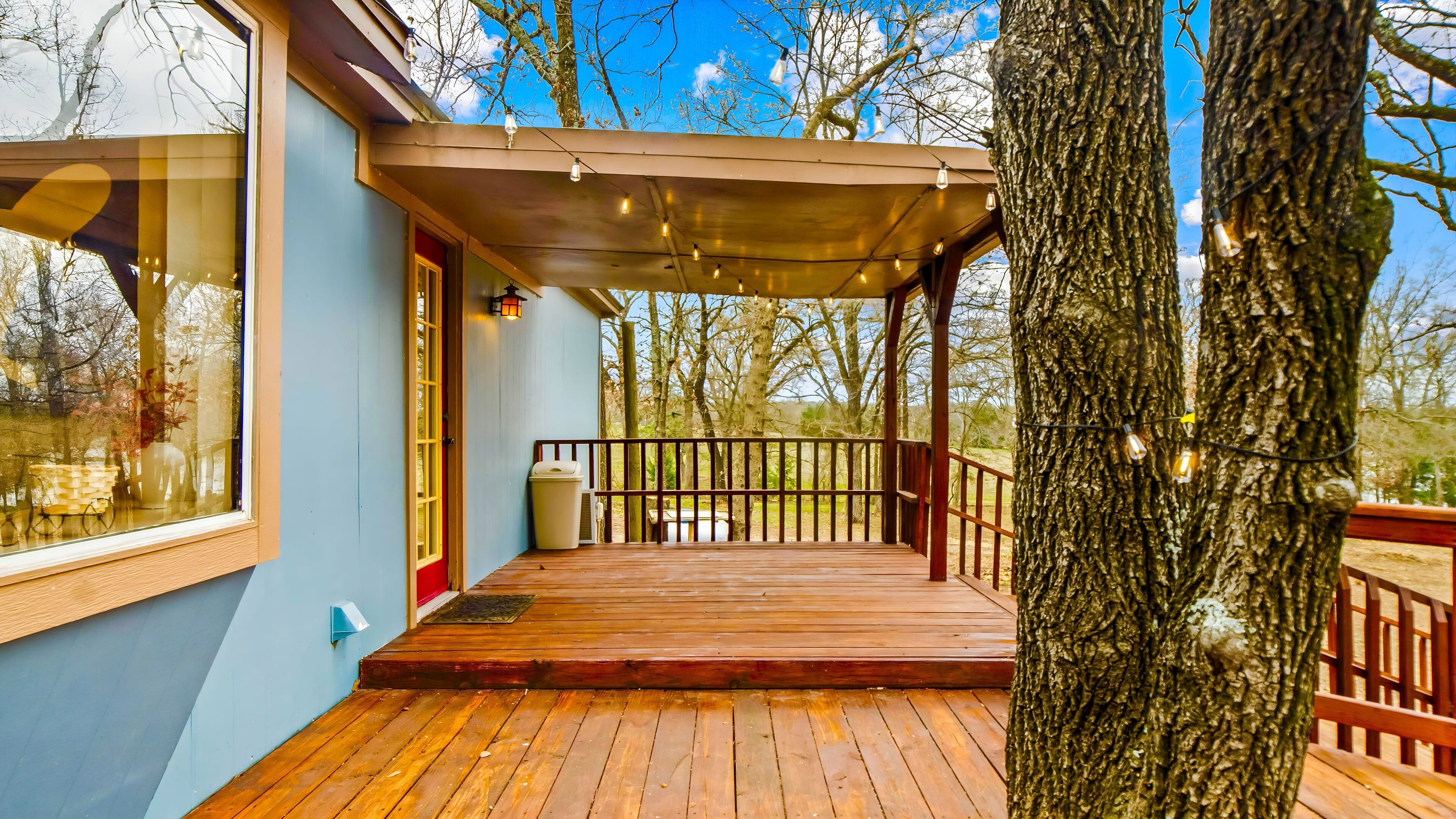 A wooden deck with a pergola, a trash bin, and a view of trees and sky.