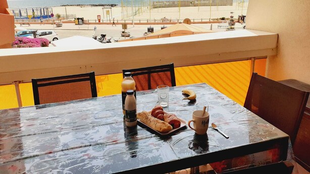 Een balkon met een ontbijttafel, met uitzicht op een strand met een hek en een pier op de achtergrond.