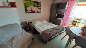 Een slaapkamer met een bed, een stoel, een bureau, een televisie en een schilderij aan de muur.