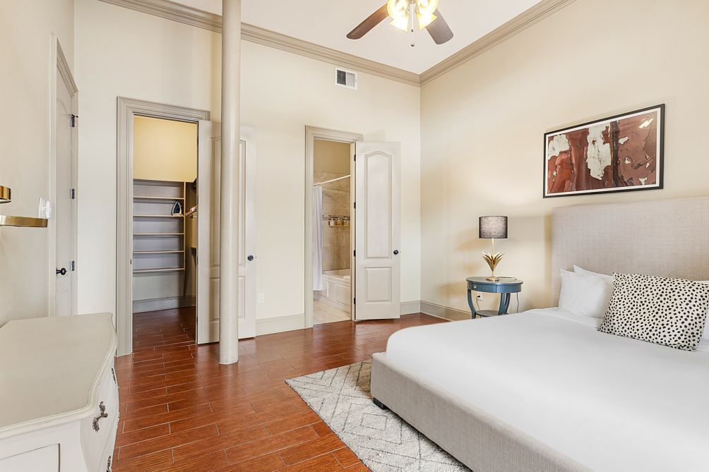 A bedroom with a bed, a nightstand, a ceiling fan, and a hallway leading to a bathroom.