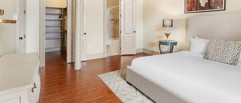 A bedroom with a bed, a nightstand, a ceiling fan, and a hallway leading to a bathroom.