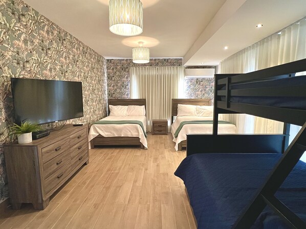 A hotel room with a wooden floor, two beds, a TV, a dresser, and a window with curtains.