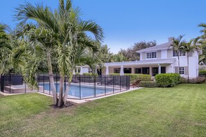 A house with a swimming pool, surrounded by well-maintained lawn and palm trees.