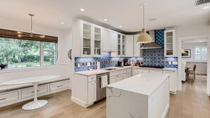 Una cocina moderna con gabinetes blancos, una isla de mármol y salpicadero de azulejos azules.