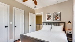 Een slaapkamer met een bed, nachtkastje, plafondventilator en twee deuren.