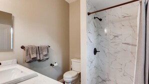 Een badkamer met een wit toilet, een wastafel met een marmeren blad en een douchegordijn met een marmer dessin.