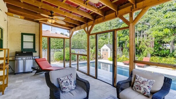 A covered outdoor area with wicker furniture, a grill, and a view of a swimming pool and greenery. - Casa del Mundo 2bd 3.5ba With Private Pool (West Palm Beach)