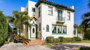 A two-story house with a white exterior, green trim, and a tiled roof. - Casa del Mundo 2bd 3.5ba With Private Pool (West Palm Beach)
