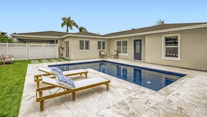 A backyard with a swimming pool, two lounge chairs, a covered patio, and a fenced area with a white fence. - Alhambra Place 4 BR 3 BA Pool Vacation Home (West Palm Beach)