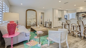 A modern living room with a sofa, a coffee table, and a large mirror. There is a kitchen area with white cabinets and a dining table with chairs. - Alhambra Place 4 BR 3 BA Pool Vacation Home (West Palm Beach)