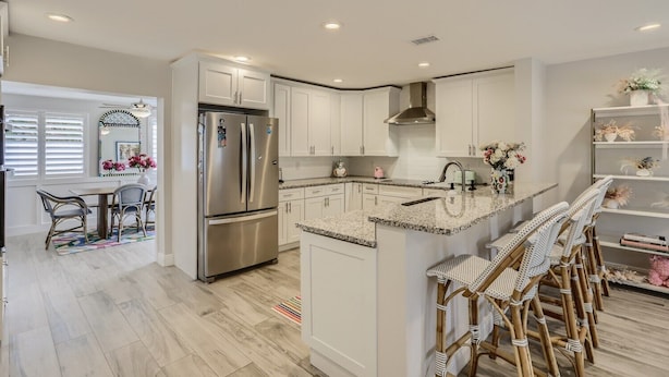 A modern kitchen with white cabinets, stainless steel appliances, and a central island with bar stools. - Alhambra Place 4 BR 3 BA Pool Vacation Home (West Palm Beach)