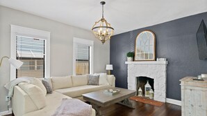A living room with a beige sofa, a wooden coffee table, a white fireplace, and a dark grey accent wall. - Casa Sunshine NEW (West Palm Beach)